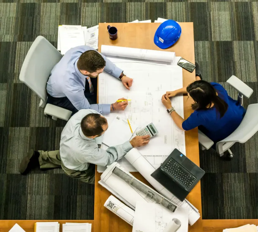 Persone discutono progetti architetturali al tavolo riunioni.